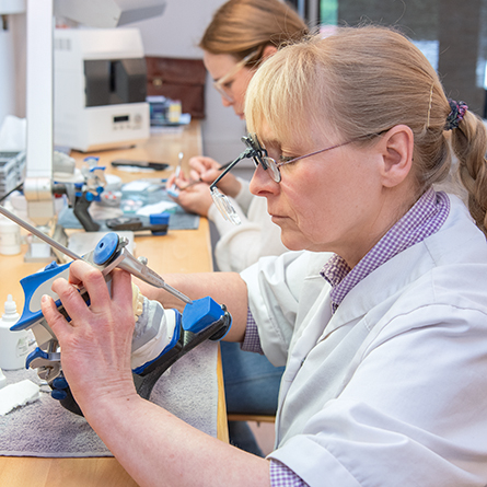 Zahntechnikerin arbeitet mit einem Artikulator an einem Zahnmodell.