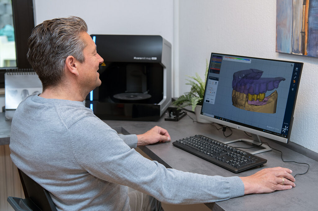 Mann sitzt vor einem Monitor mit digitalem Zahnmodell in 3D-Software.