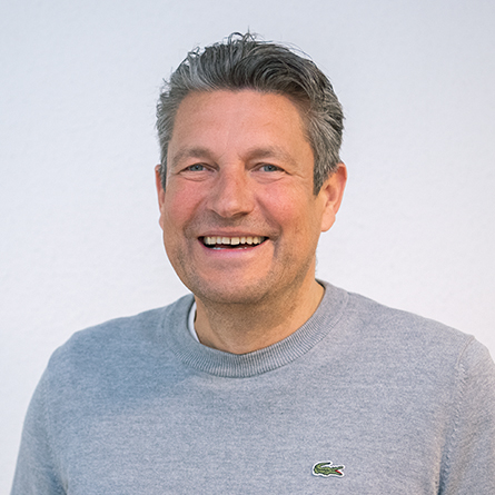 Porträt eines Mannes mit grauem Pullover, der freundlich in die Kamera lächelt.