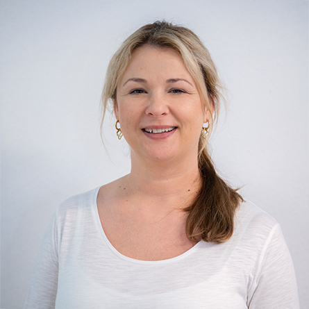 Porträt einer Frau mit hellem Oberteil und Pferdeschwanz, die in die Kamera lächelt.