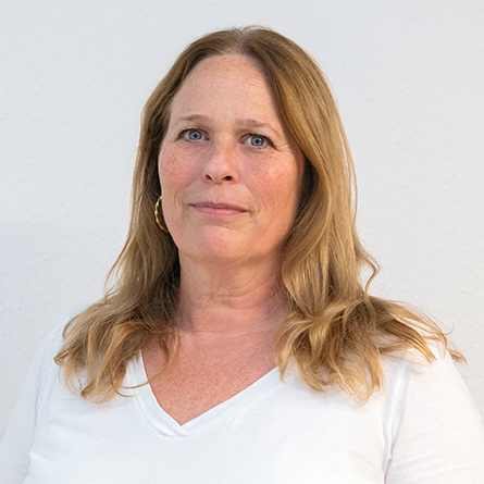 Frau mit langen, blonden Haaren und weißem Shirt blickt freundlich in die Kamera.